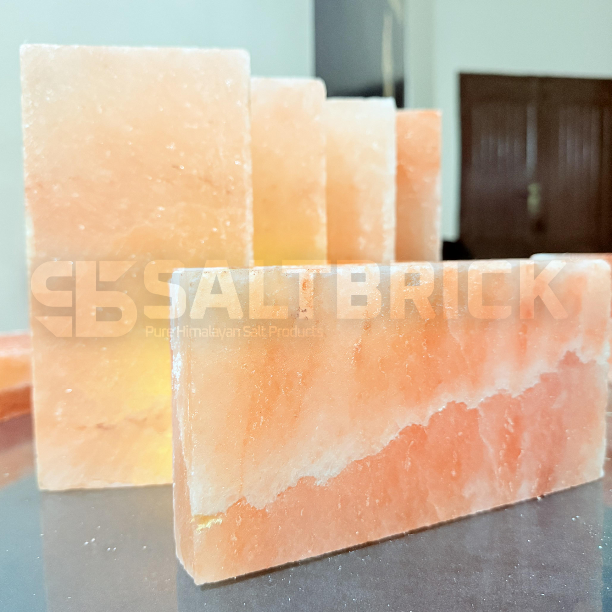 Three pink Himalayan salt bricks on a reflective surface with a blurred background.