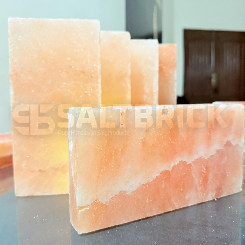 Three pink Himalayan salt bricks on a reflective surface with a blurred background.